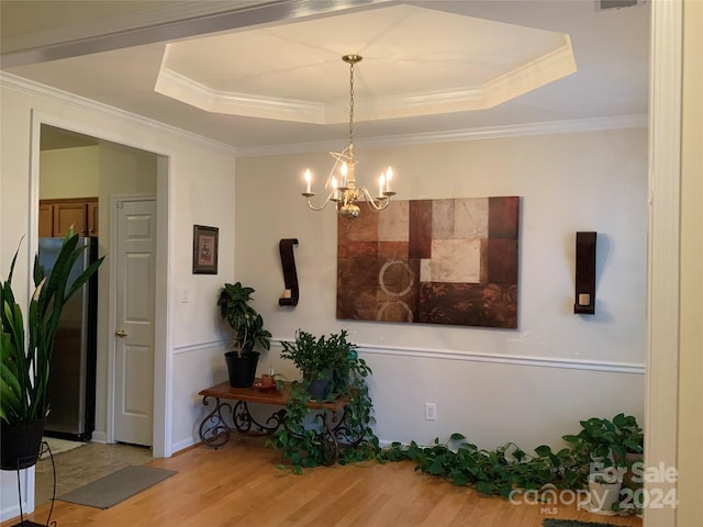 dining area with crown molding, a raised ceiling, an inviting chandelier, and hardwood / wood-style floors