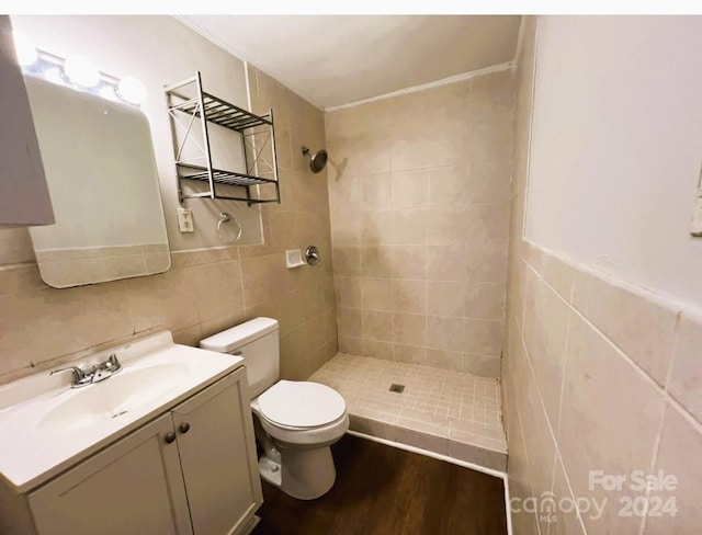 bathroom with tile walls, vanity, a tile shower, wood-type flooring, and toilet