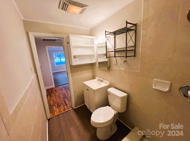 bathroom with tile walls, hardwood / wood-style floors, crown molding, vanity, and toilet