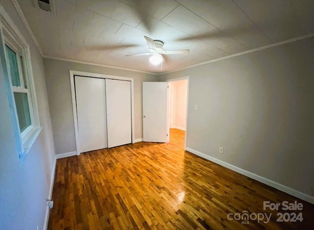 unfurnished bedroom featuring a closet, wood-type flooring, ceiling fan, and crown molding