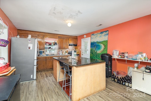 kitchen with light hardwood / wood-style floors, sink, a kitchen island, a kitchen breakfast bar, and stainless steel appliances