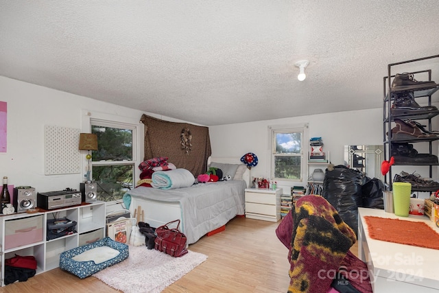 bedroom featuring a textured ceiling, light hardwood / wood-style floors, and multiple windows