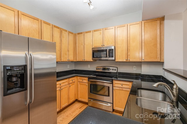 kitchen featuring stainless steel appliances, light brown cabinetry, light hardwood / wood-style flooring, track lighting, and sink