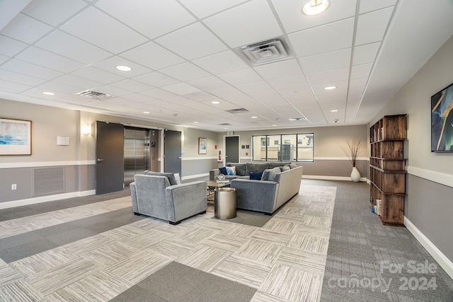 carpeted living room with a drop ceiling and elevator