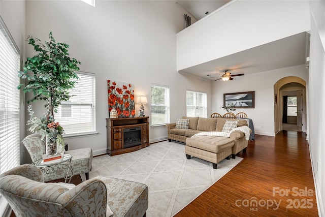 living room with plenty of natural light, light hardwood / wood-style floors, ceiling fan, and a high ceiling