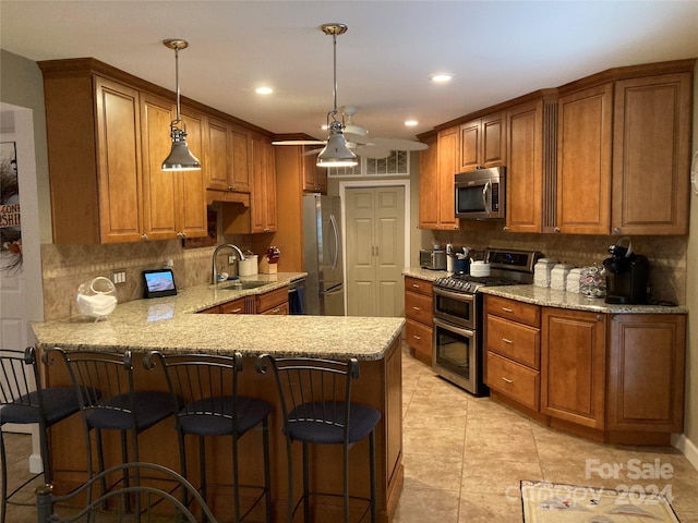 kitchen featuring hanging light fixtures, sink, kitchen peninsula, appliances with stainless steel finishes, and light stone countertops