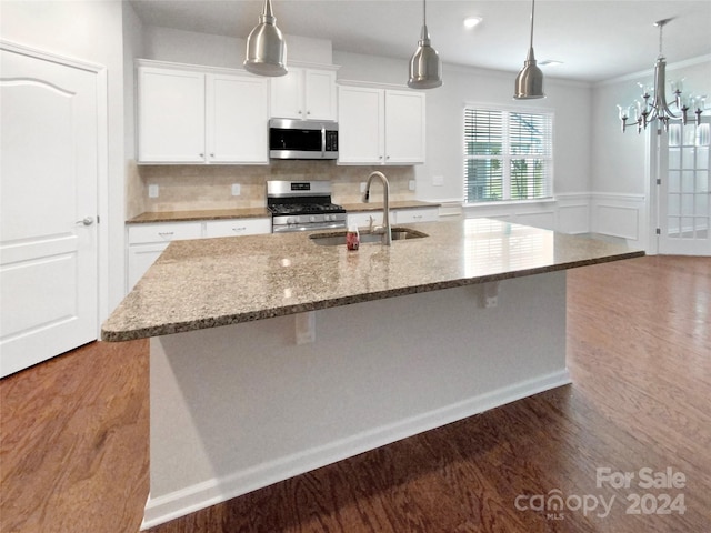 kitchen with hanging light fixtures, dark stone countertops, white cabinets, stainless steel appliances, and a center island with sink