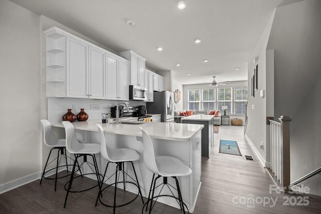 kitchen featuring kitchen peninsula, appliances with stainless steel finishes, tasteful backsplash, sink, and white cabinetry