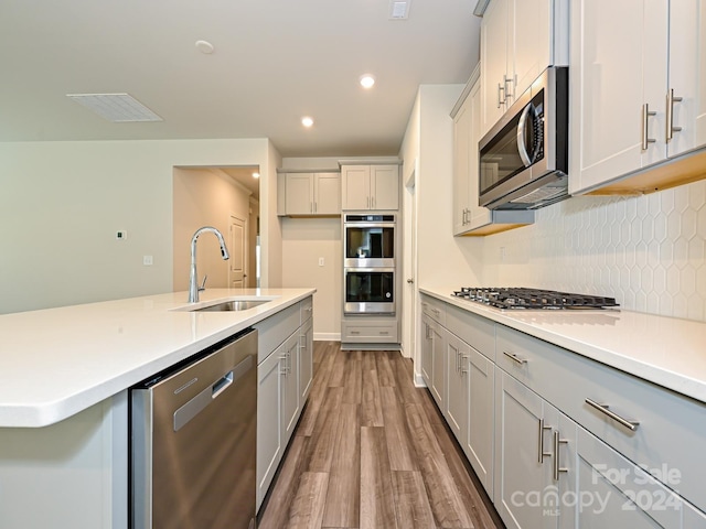 kitchen with appliances with stainless steel finishes, backsplash, sink, and light hardwood / wood-style flooring