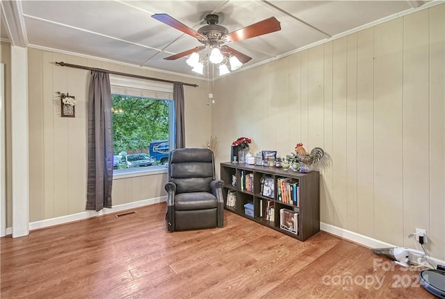 sitting room with wood walls, ceiling fan, hardwood / wood-style flooring, and crown molding