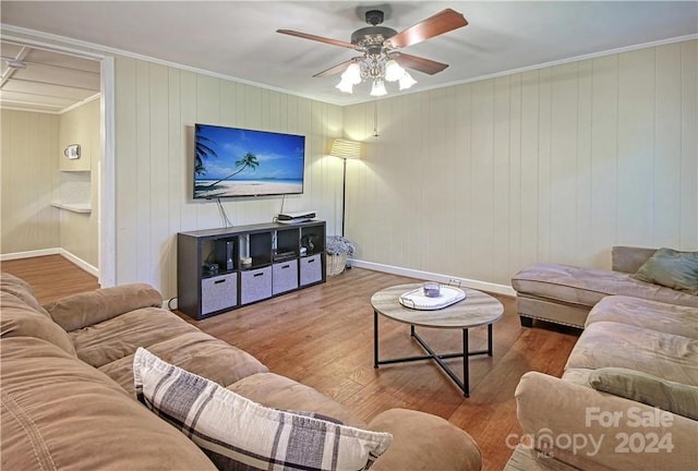 living room with ornamental molding, wood-type flooring, ceiling fan, and wooden walls