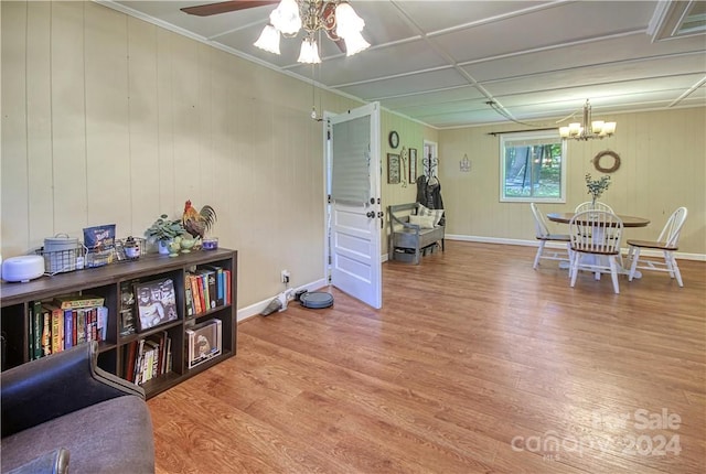 sitting room featuring ceiling fan with notable chandelier, wooden walls, hardwood / wood-style floors, and ornamental molding