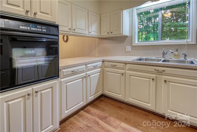 kitchen featuring black oven, light hardwood / wood-style floors, backsplash, and sink