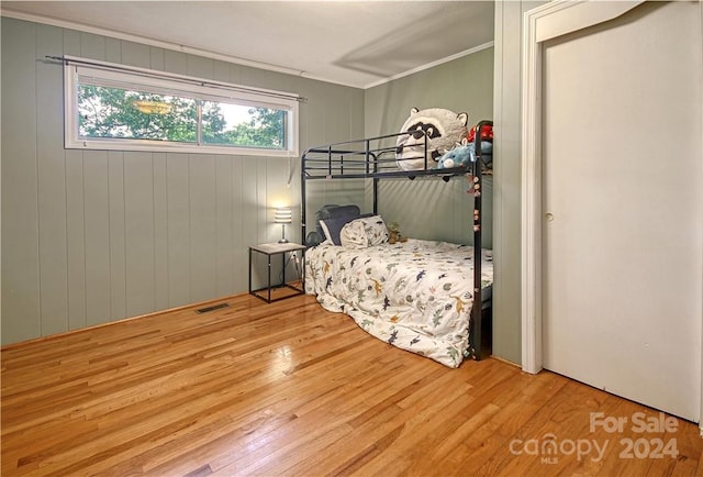 bedroom featuring wood walls, hardwood / wood-style flooring, and crown molding