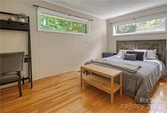 bedroom with light hardwood / wood-style flooring, wooden walls, a fireplace, and crown molding