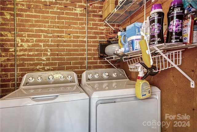 laundry area featuring brick wall and washer and dryer