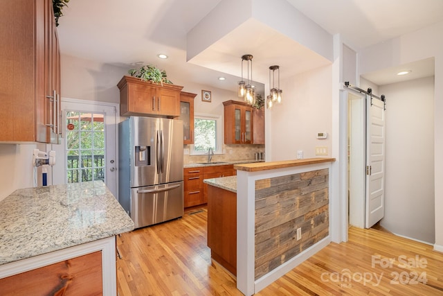 kitchen with light hardwood / wood-style floors, a barn door, decorative light fixtures, and stainless steel fridge