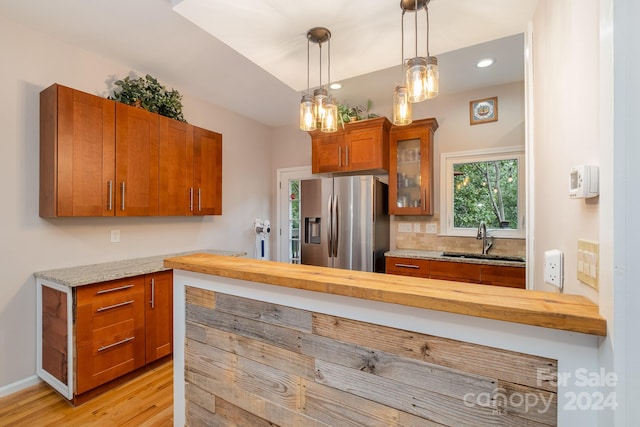 kitchen with wooden counters, light wood-type flooring, decorative light fixtures, stainless steel refrigerator with ice dispenser, and sink