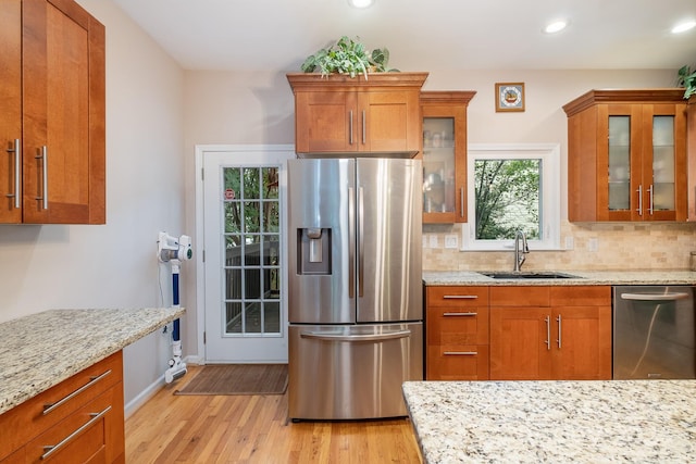 kitchen with light stone counters, appliances with stainless steel finishes, light wood-type flooring, and sink