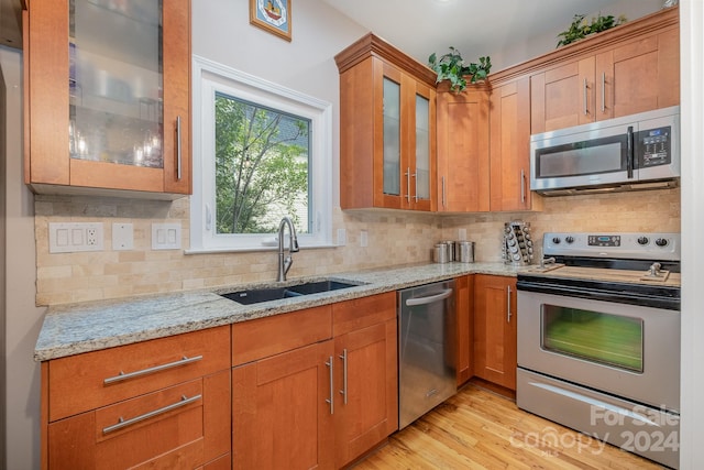 kitchen featuring appliances with stainless steel finishes, backsplash, sink, and light hardwood / wood-style flooring