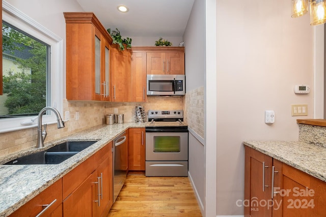 kitchen with appliances with stainless steel finishes, backsplash, light hardwood / wood-style floors, and light stone countertops