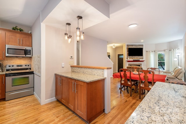 kitchen with light stone counters, tasteful backsplash, decorative light fixtures, stainless steel appliances, and light wood-type flooring