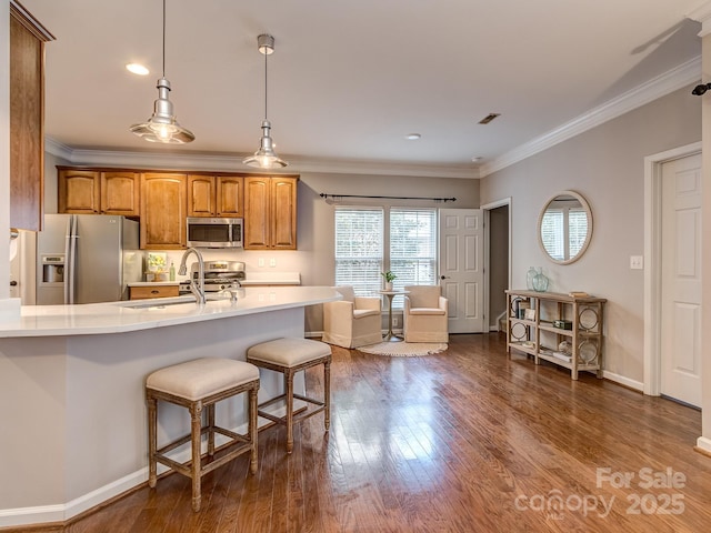 kitchen featuring crown molding, appliances with stainless steel finishes, a kitchen bar, dark hardwood / wood-style flooring, and decorative light fixtures