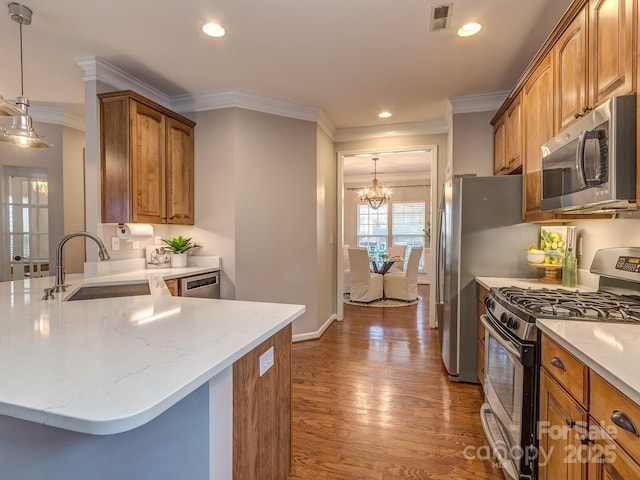 kitchen with appliances with stainless steel finishes, pendant lighting, wood-type flooring, sink, and an inviting chandelier