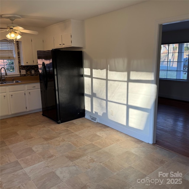 kitchen with backsplash, black refrigerator with ice dispenser, ceiling fan, sink, and white cabinets