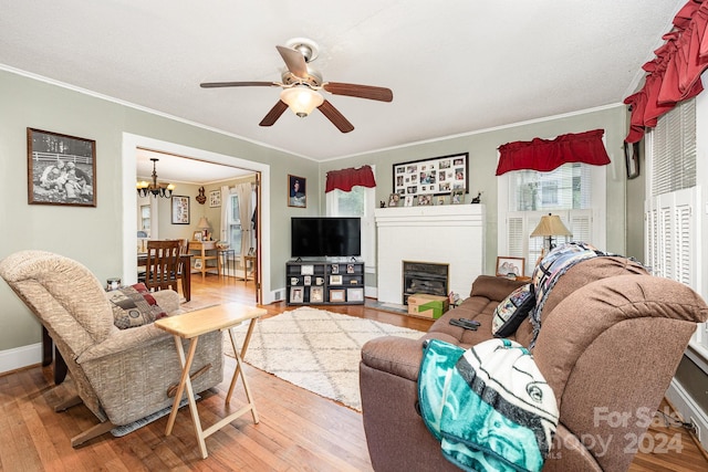 living room with ceiling fan with notable chandelier, ornamental molding, hardwood / wood-style floors, and a brick fireplace