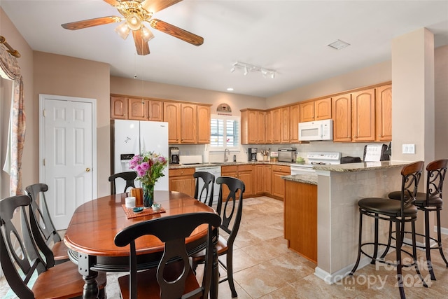 kitchen with white appliances, kitchen peninsula, light stone countertops, ceiling fan, and sink