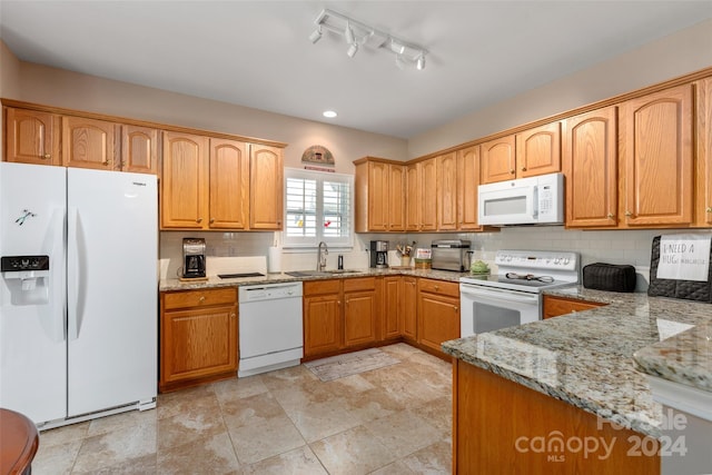 kitchen featuring light stone counters, track lighting, sink, backsplash, and white appliances