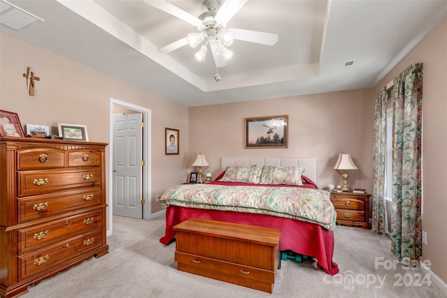 bedroom with ceiling fan, light colored carpet, and a tray ceiling