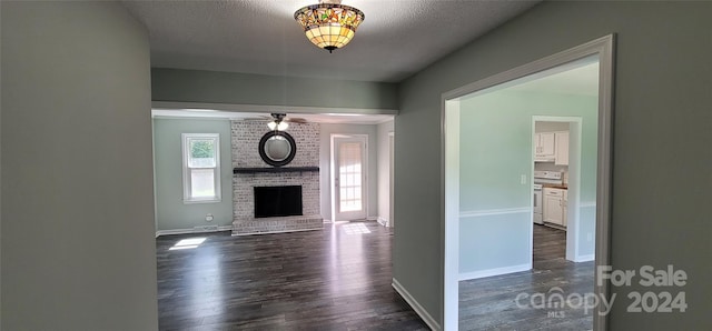 unfurnished living room featuring a textured ceiling, dark hardwood / wood-style flooring, ceiling fan, and a brick fireplace