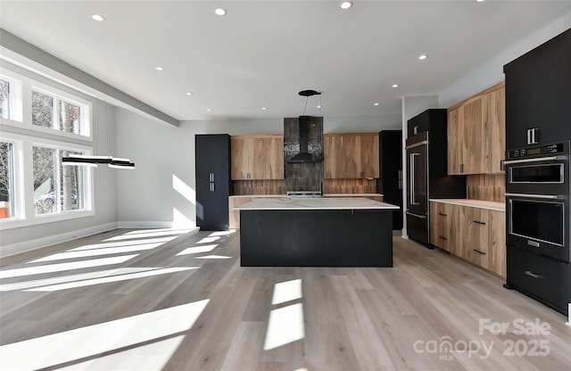 kitchen featuring a center island, decorative backsplash, light wood-type flooring, decorative light fixtures, and wall chimney exhaust hood