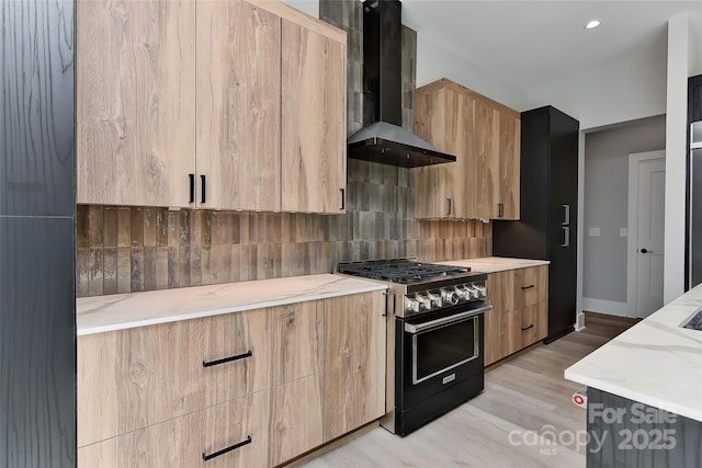 kitchen featuring tasteful backsplash, light stone countertops, range with two ovens, wall chimney range hood, and light hardwood / wood-style floors