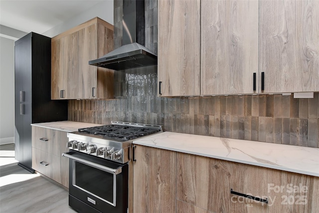 kitchen with decorative backsplash, wall chimney range hood, light wood-type flooring, high end stainless steel range oven, and light stone counters