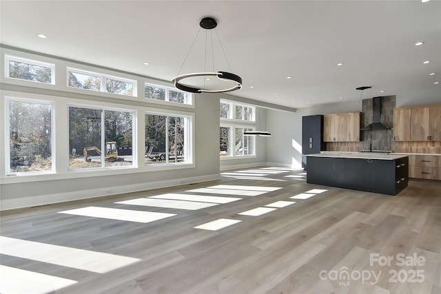 interior space with hanging light fixtures, wall chimney exhaust hood, tasteful backsplash, a center island, and light hardwood / wood-style floors