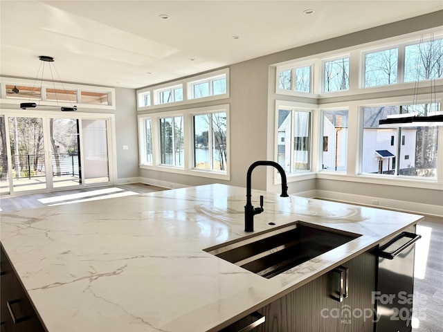 kitchen featuring stainless steel dishwasher, hanging light fixtures, sink, light stone counters, and a kitchen island