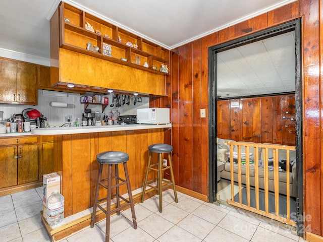 kitchen with wooden walls, light tile patterned floors, kitchen peninsula, and a kitchen breakfast bar