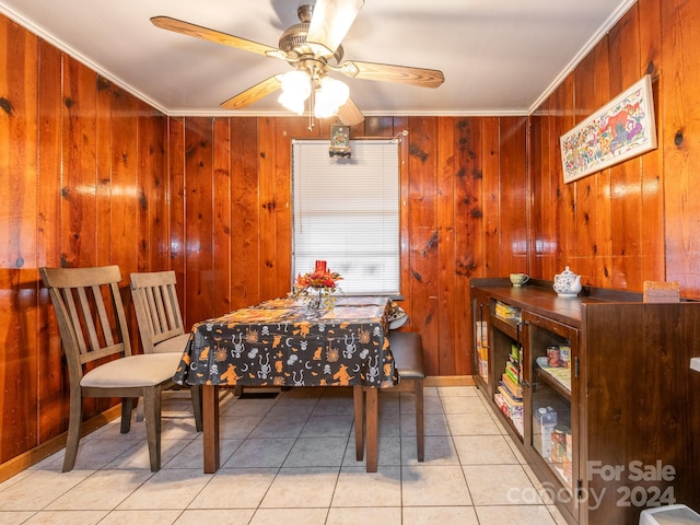 dining space with crown molding, wood walls, light tile patterned floors, and ceiling fan