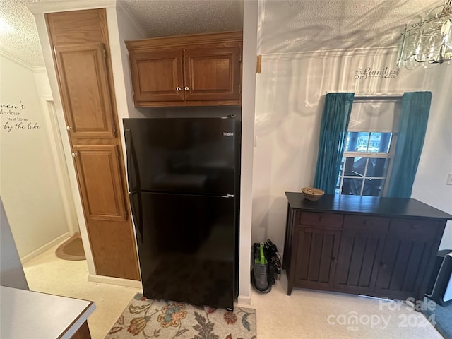 kitchen with a textured ceiling, light colored carpet, black fridge, and crown molding