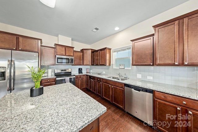 kitchen with light stone countertops, dark wood-type flooring, stainless steel appliances, and tasteful backsplash