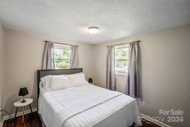 bedroom with a textured ceiling, dark hardwood / wood-style floors, and multiple windows