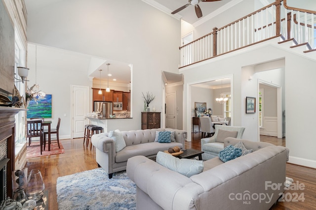 living room with light wood-type flooring, crown molding, a high ceiling, and ceiling fan with notable chandelier