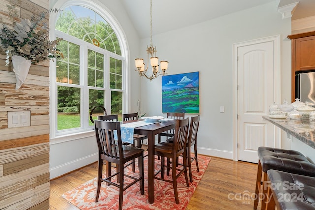 dining space with light hardwood / wood-style flooring, lofted ceiling, a notable chandelier, and a healthy amount of sunlight