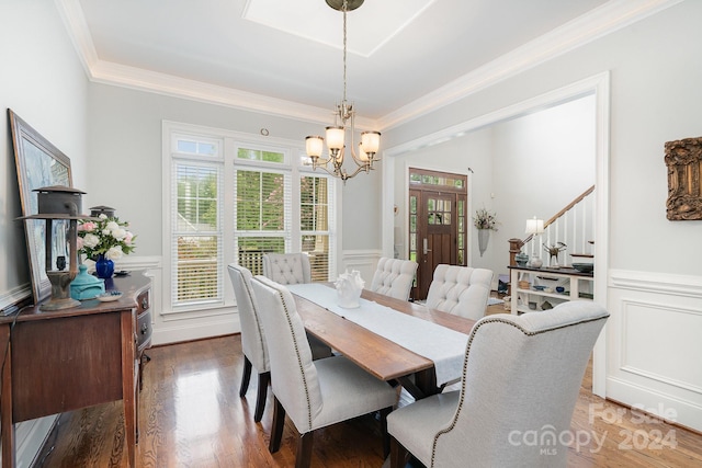 dining area with wood-type flooring, an inviting chandelier, and crown molding