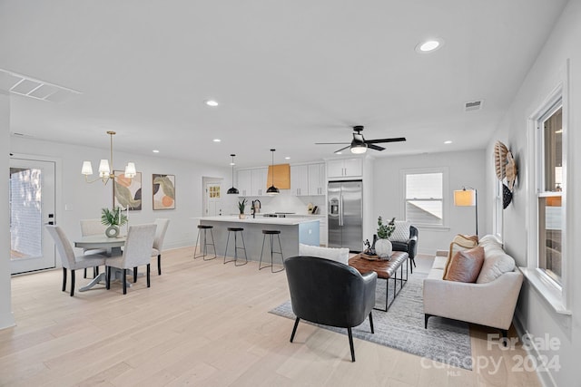 living room with ceiling fan with notable chandelier, light wood-type flooring, and sink