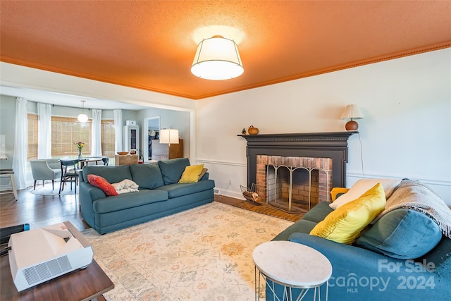 living room featuring a textured ceiling, wood-type flooring, crown molding, and a brick fireplace