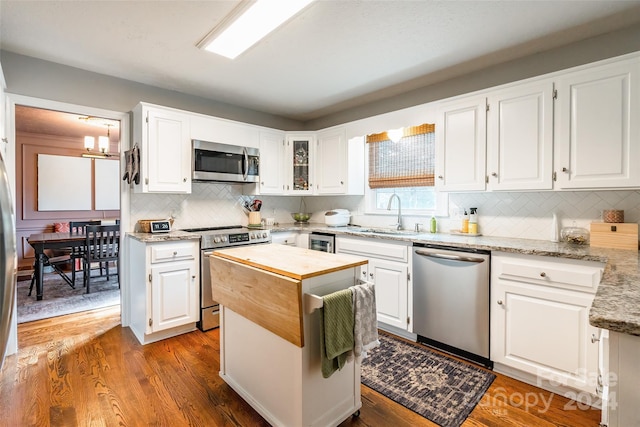 kitchen with wood-type flooring, light stone counters, stainless steel appliances, sink, and white cabinets